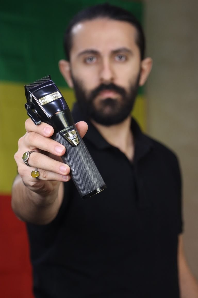 Man holding a cordless beard trimmer with a dark, tapered head against a black shirt.