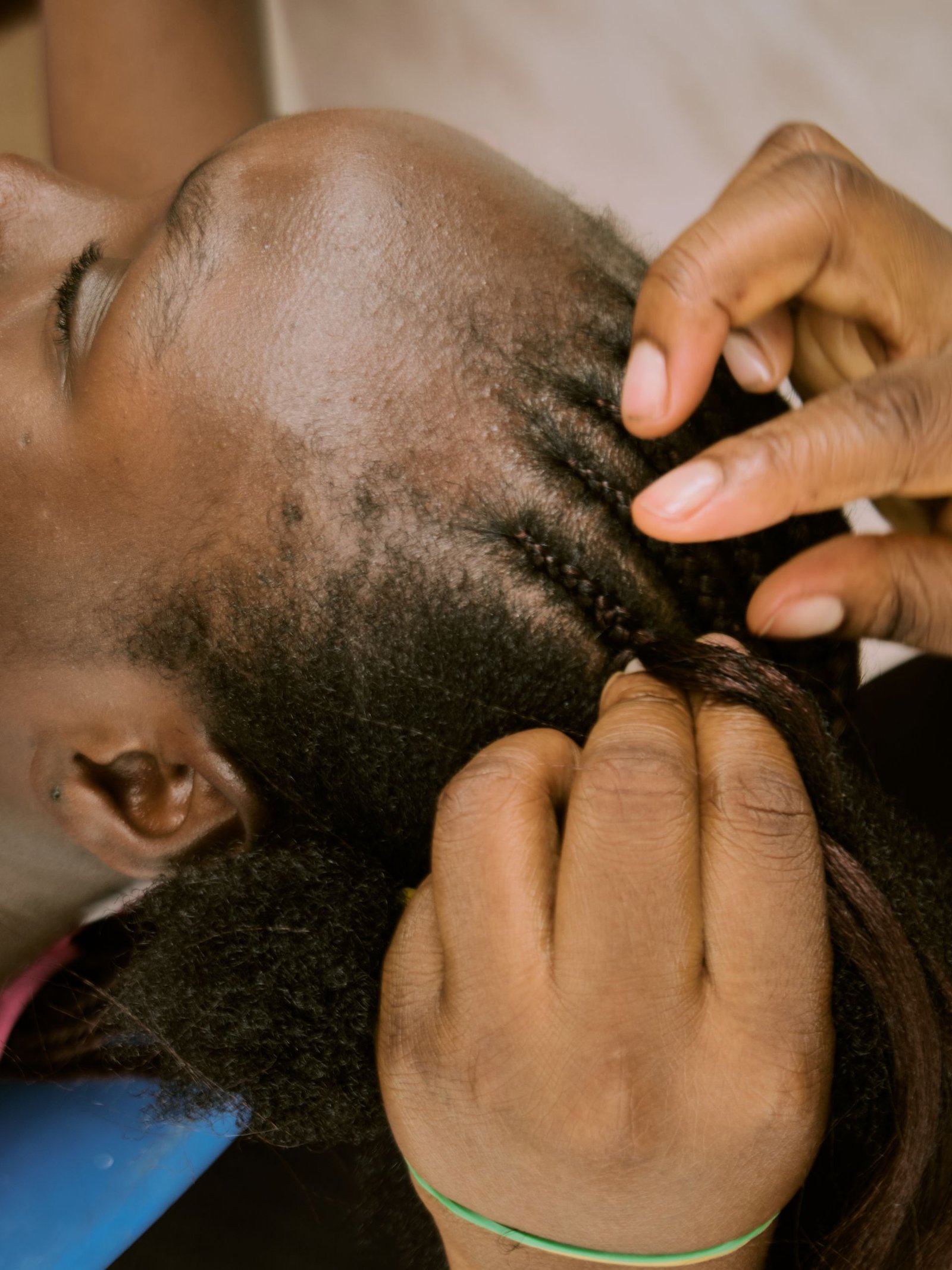 Braider working hair into a cornrow section along the scalp