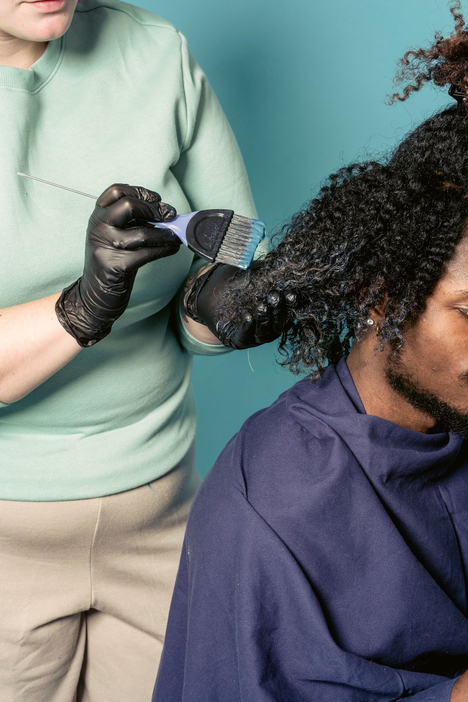 Hairstylist applying a perm solution to a man's curly hair during a salon appointment