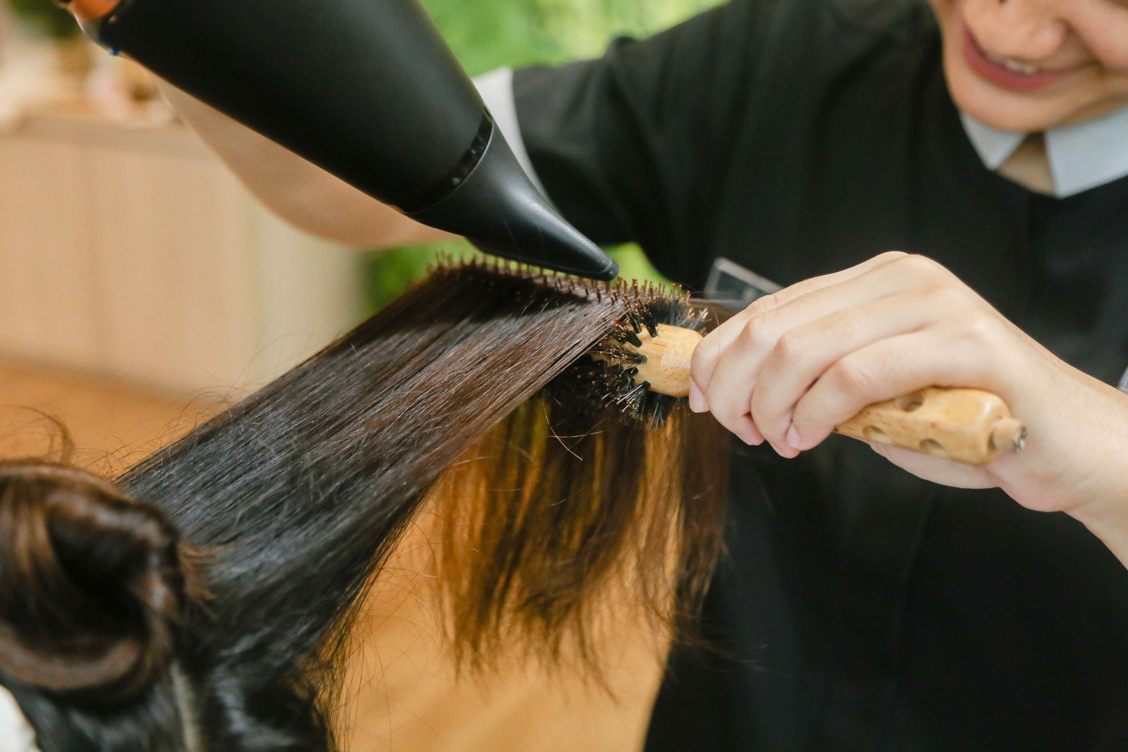 Hairstylist sectioning damp hair and wrapping it around a round brush before blow-drying