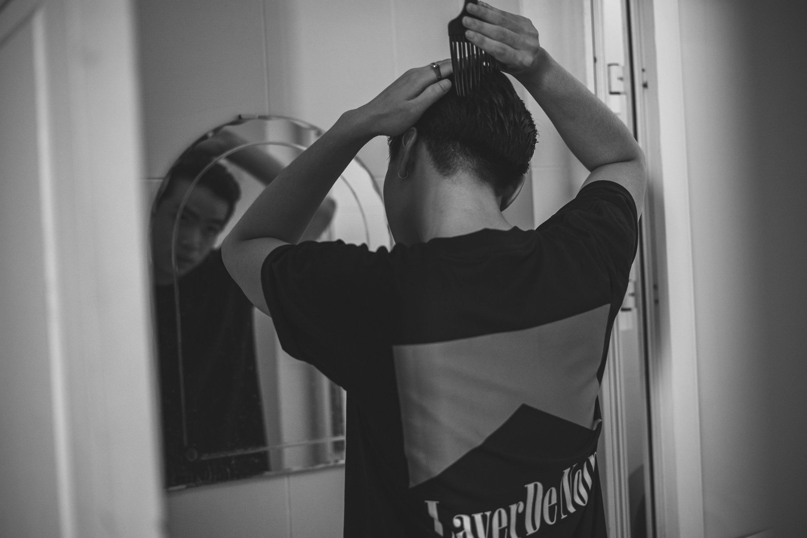 Man combing his hair into a classic side part in front of a mirror