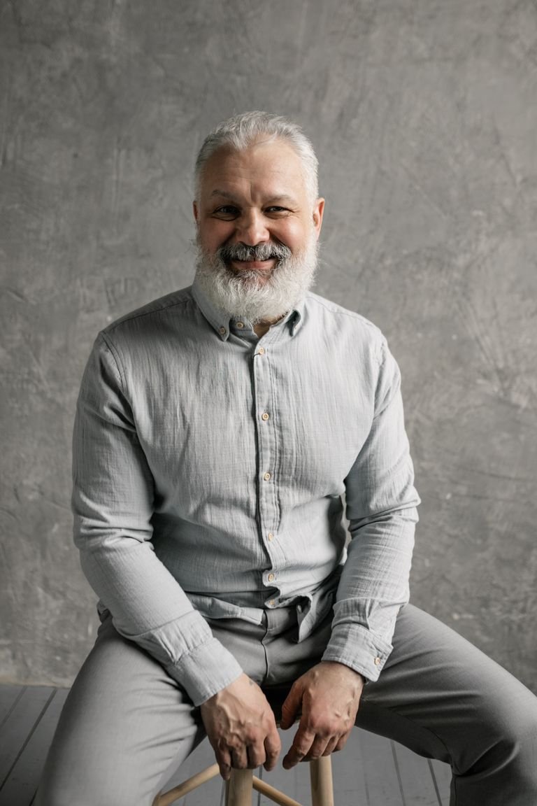 Smiling older man with a full gray beard and short gray hair, an example of a classic hairstyle and beard pairing for mature men.