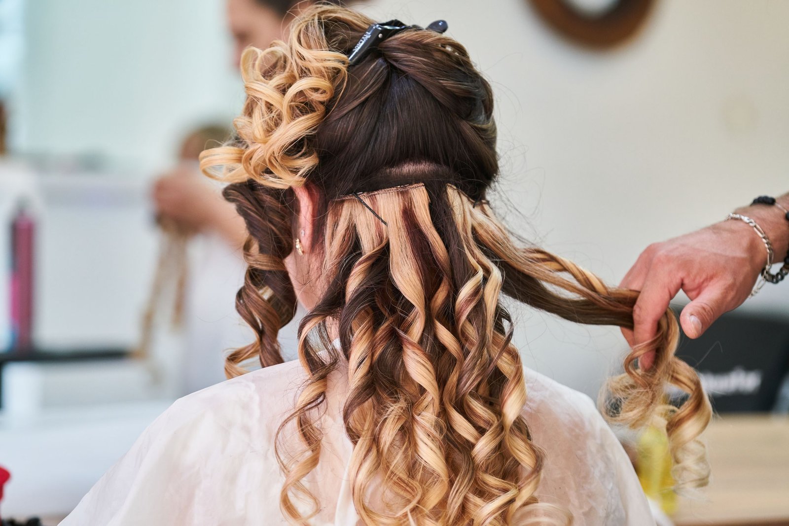 Stylist working on a woman's hair, blending extensions into her natural hairstyle.