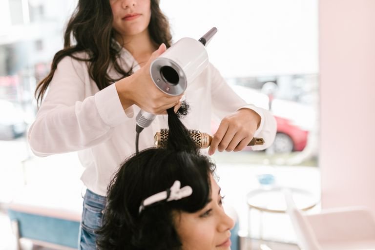 Woman blow-drying her own hair at home with a round brush to create a smooth blowout