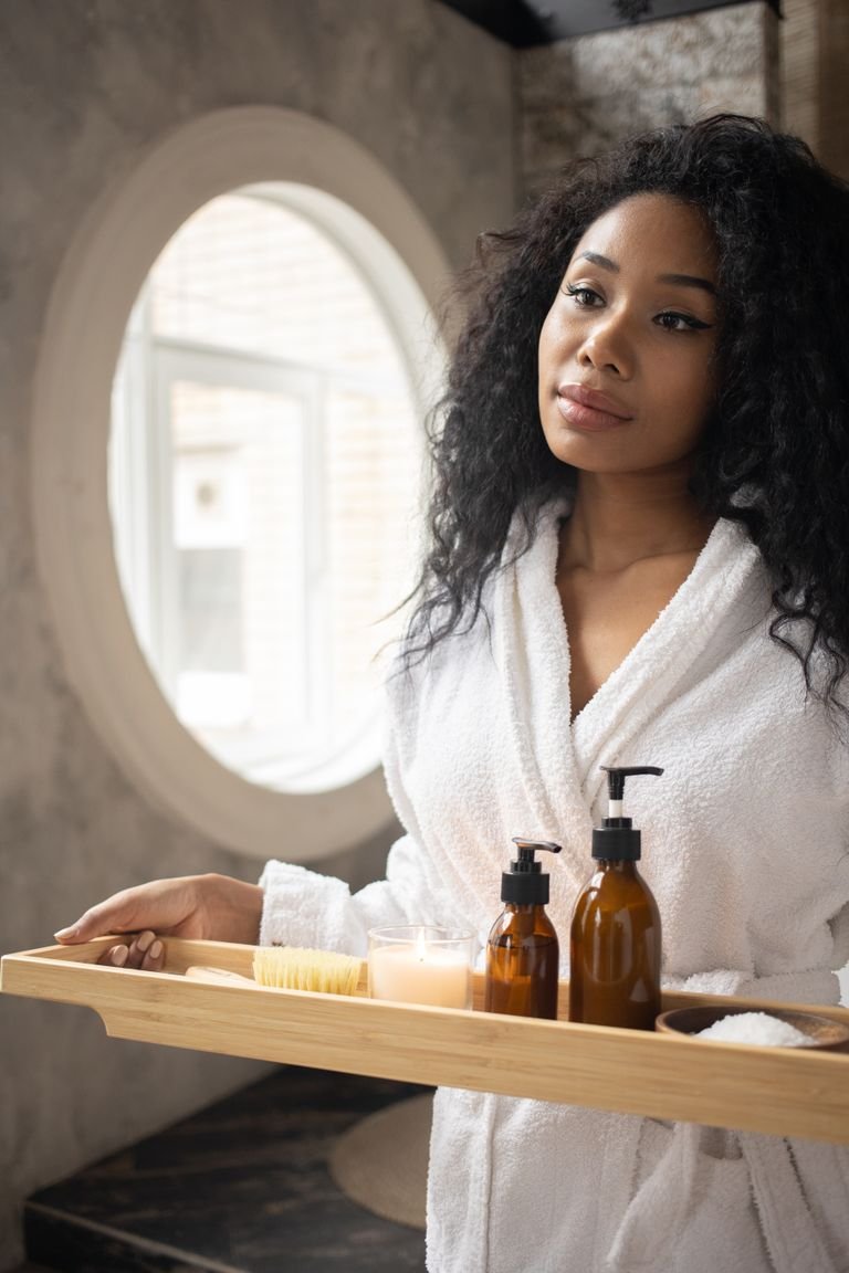 Woman in a bathrobe holding shampoo bottles in a bright bathroom
