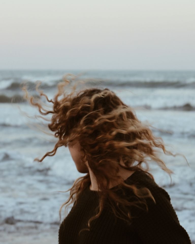 Woman with loose beach waves in her hair standing by the sea