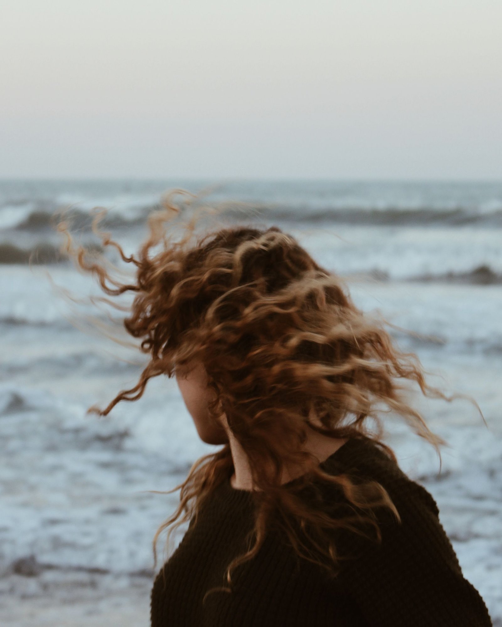 Woman with loose beach waves in her hair standing by the sea