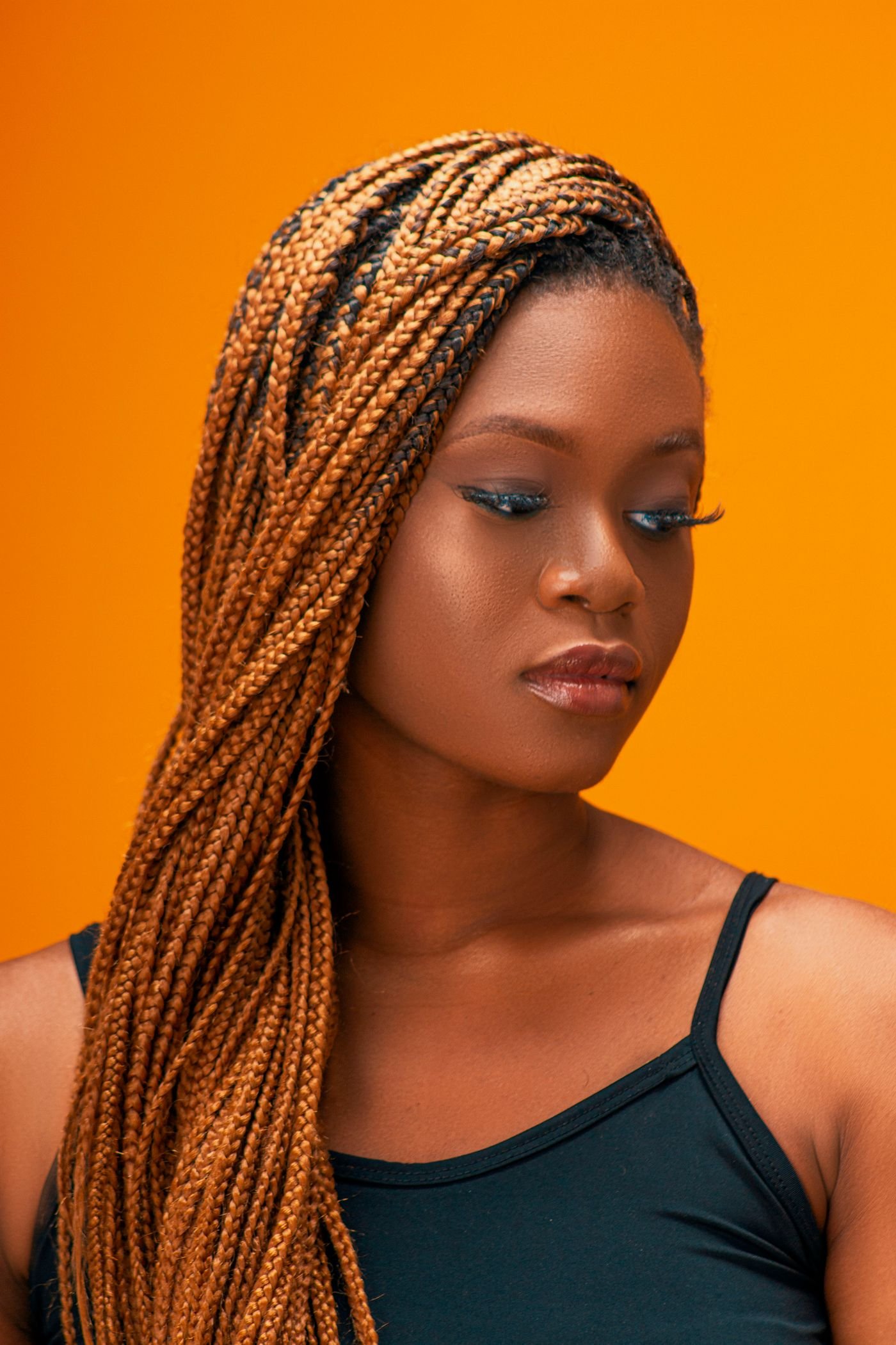 Portrait of a woman with box braids against a vivid orange backdrop