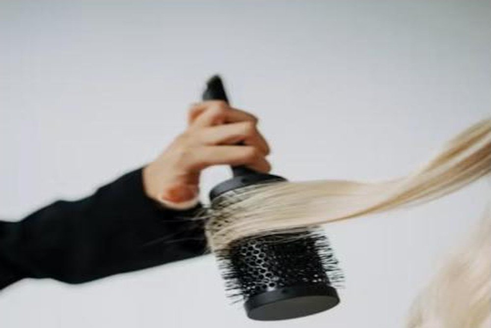 Close-up of a round brush styling long blonde hair strand by strand