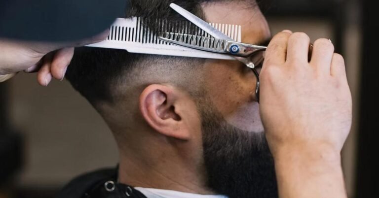 Barber using thinning scissors and comb to cut a man's short faded haircut