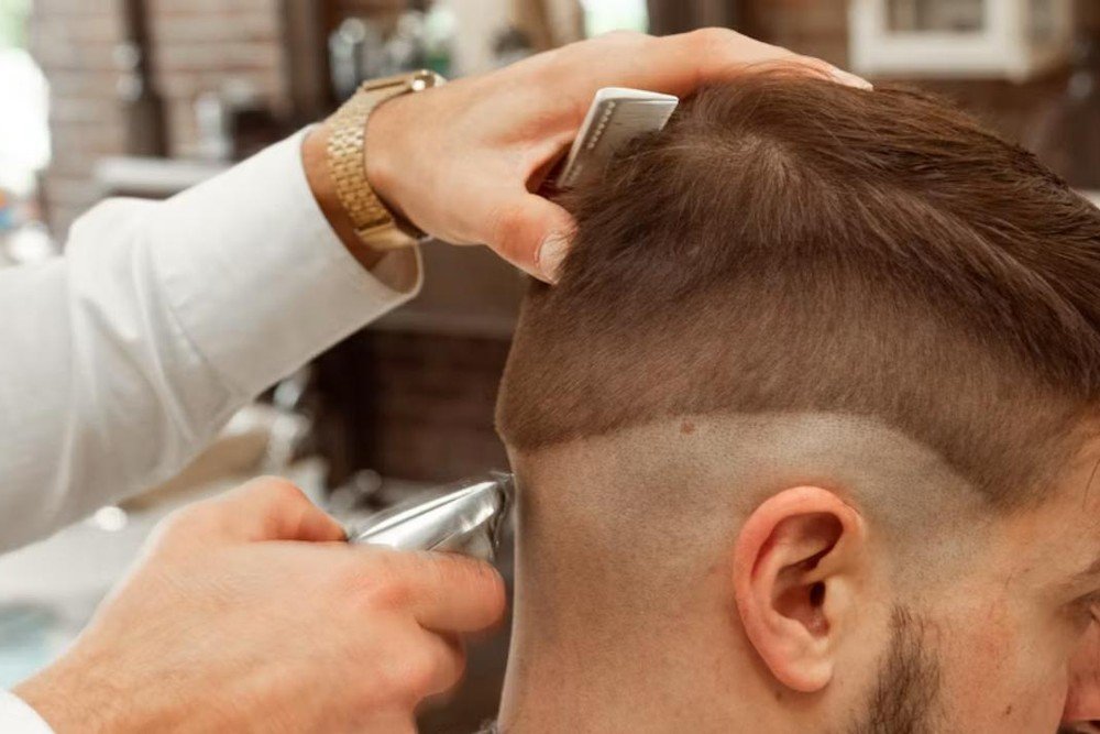 Barber using clippers to shape the tapered nape of a men's buzz cut