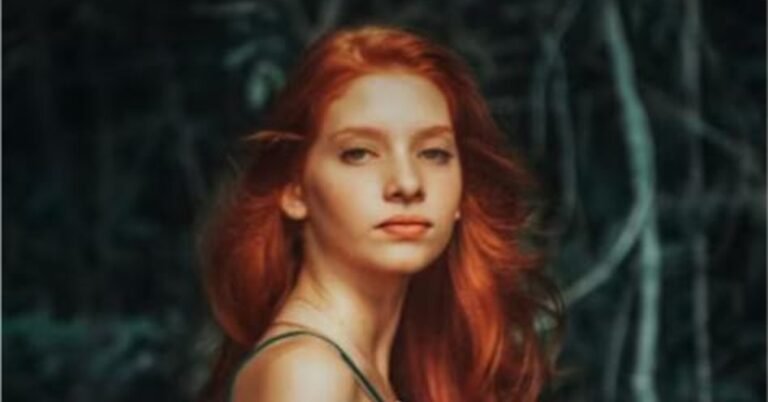 Woman with deep red hair against a dark background, an example of the red and black hair color trend