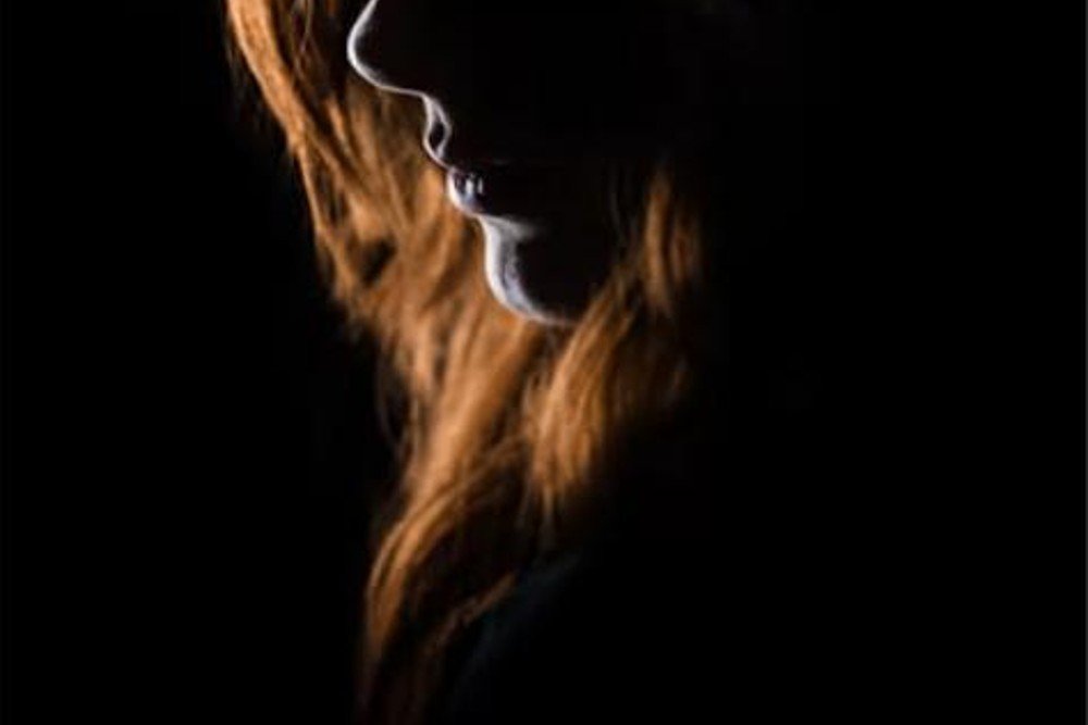 Close-up silhouette of deep red hair lit against a solid black background, showing the rich red-on-black contrast at the center of this color trend